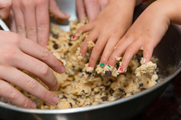 Many hands in the pot making cookie dough with a shallow depth of field