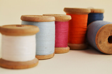Fototapeta na wymiar Old wooden spools with multicolored cotton threads on a light background.