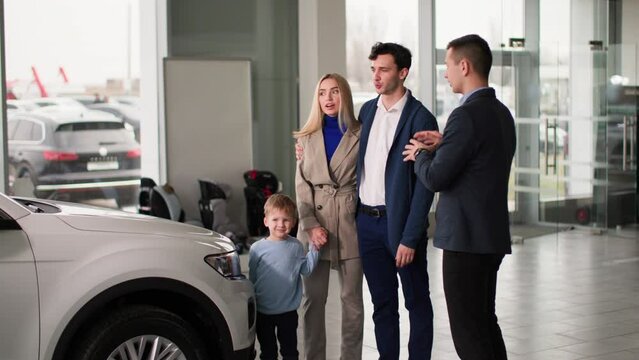 buying car, a young married couple with a son consults with manager in auto dealership about vehicle for family