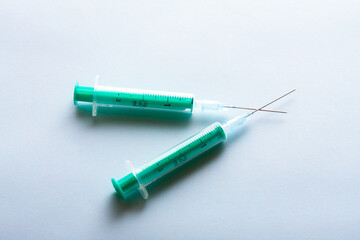A pair of green medical syringes on bright blue background.