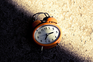 Vintage style orange alarm clock under the bright light and dark shadow.