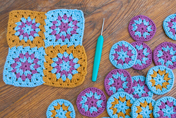 Top view of crochet hook and crochet granny squares and circles on vintage wooden surface.