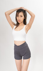Portrait of a young and sexy beautiful asian female lady model with nice body shape wearing white tops and grey pants for indoor exercise