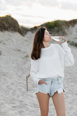 Side view of young woman drinking mineral water on beach.