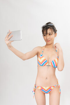 Portrait of a young and attractive sexy asian female lady model wearing colorful summer bikini talking, selfie, video call and chit chat over a mobile phone