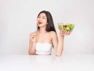 Portrait of a young and smart asian female lady wearing white tank top with different look & poses and big happy smiles, holding a bowl of salad vegetables against a white studio backdrop