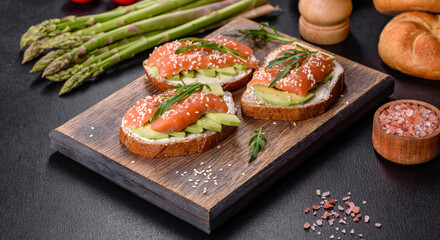 Toast sandwich with butter, avocado and salmon, decorated with arugula and sesame seeds, on a black stone background