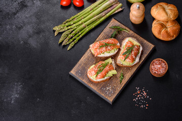 Toast sandwich with butter, avocado and salmon, decorated with arugula and sesame seeds, on a black stone background