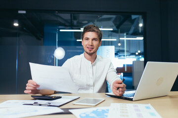 Portrait of a successful businessman at paper work, man smiling and looking at camera holding document and financial reports