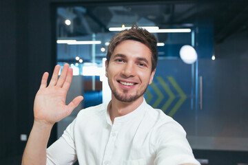 A young businessman in a shirt and beard looks into the camera of a smartphone talking happily on a...