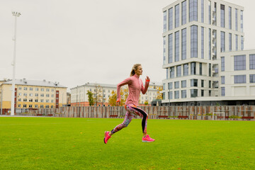 Running training at the stadium. A young woman in a bright tracksuit practicing running technique