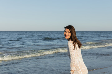 Fototapeta na wymiar Happy brunette woman looking at camera near blurred sea.
