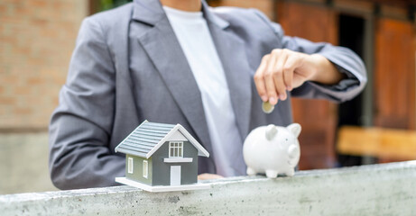 Businesswomen hold piggy banks and put coins in piggy banks to save money with coins to step into business real estate. Savings and real estate concept