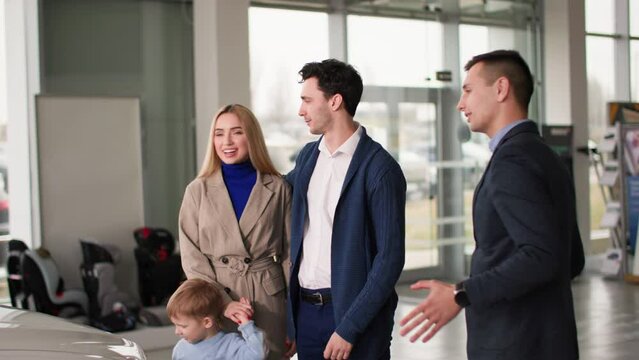 auto shop, male manager showing happy buyers with child new family car in mall