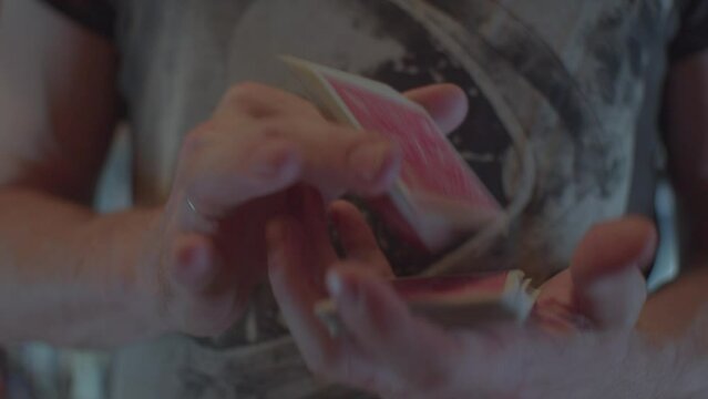 Man's hands are shuffling a deck of cards with a red back