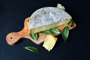 Saint Nectaire cheese with bay leaf on a cutting board. It is an Auvergne cheese and a mountain...