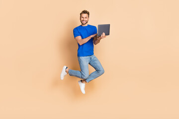 Full size photo of excited energetic person use wireless netbook jumping isolated on beige color background