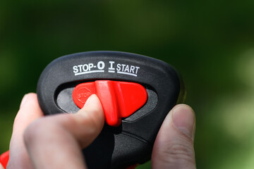 Close-up worker switches the button on the gas trimmer handle, lawn mowers on a green background....