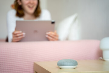 Smart ai speaker in living room. Blurred out woman in background talking to voice device.