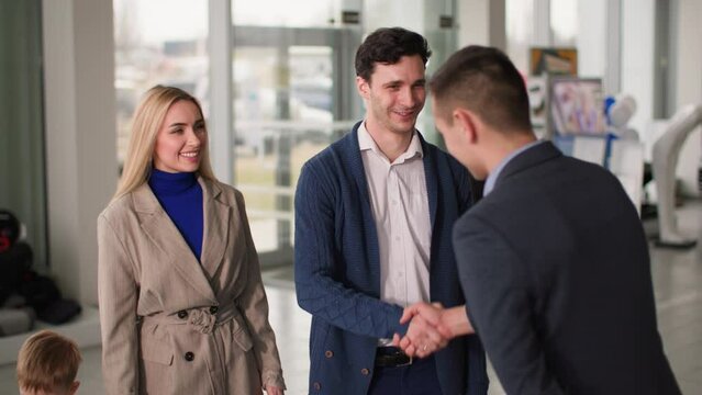 dealership, joyful man with wife and son shaking hands with car dealership manager, happy family chatting with seller about buying a car at sales center