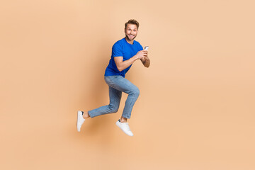 Fototapeta na wymiar Full size profile side photo of young guy jump use mobile blogger app button isolated over beige color background