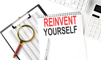 Office desk table with keyboard, notepad ,chart and calculator. Top view with text REINVENT YOURSELF