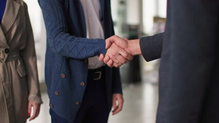 successful purchase of a vehicle, satisfied buyers shake hands with a male seller after buying a new car in auto salon, close-up