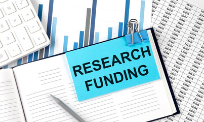 RESEARCH FUNDING on sticky note on notebook on the chart background