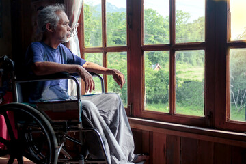 An Asian senior man sat in a wheelchair and looked at the window waiting for his family.