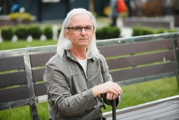 Fototapeta premium Portrait of senior man holding walking stick while resting in park.