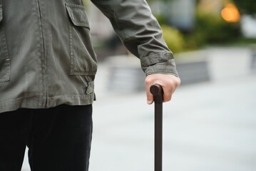 Elderly man walks with a cane in a city spring park.