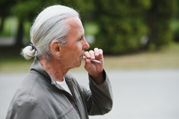 An old senior man smoking cigarette outside, smoke addiction, bad habbit