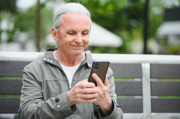 Old man browsing app on smartphone, outdoor in park