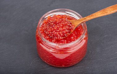 Wooden spoon with red caviar in a glass jar with caviar.