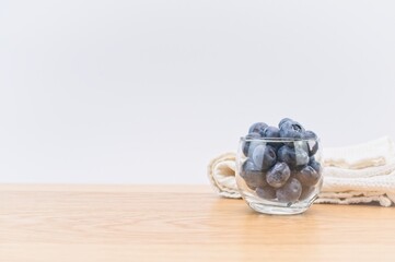 glass bowl with fresh organic blueberries and white kitchen towel on a bright wooden table
