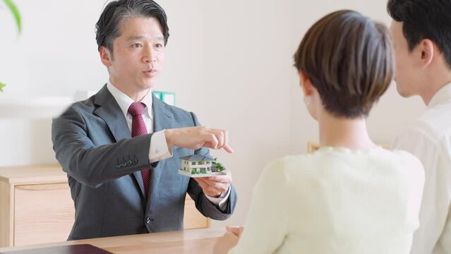家の模型を使って説明するビジネスマンと日本人男女