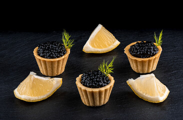 Tartlets with black caviar and slices of lemon on a stone board for serving.
