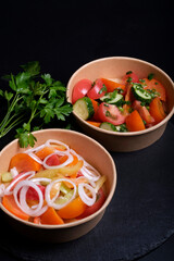 vegetable salad in a cardboard plate tomato cucumber greens on a black background food delivery still life