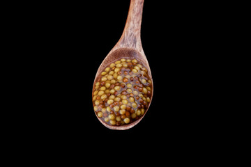 Wooden spoon full of french mustard isolated on black background.
