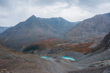 Awesome aerial view to turquoise eyes-lakes and pyramid shaped high mountain under dramatic gray cloudy sky. Two beautiful mountain lakes among fading autumn colors in overcast. Small glacial lakes.