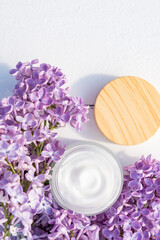 Obraz na płótnie Canvas Jar of cream and lilac flowers on a white background, top view. Professional cosmetic products. Beauty and health concept. Plant-based cosmetics