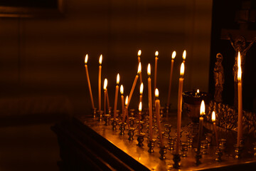 Fototapeta na wymiar Memorial candles for the dead burn on the altar in the darkness of the temple next to the crucifixion of Jesus Christ, the concept of eternal memory of the departed