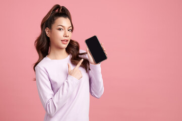 Naklejka premium Beautiful young asian women pointing at blank screen of smart phone, on pink background,