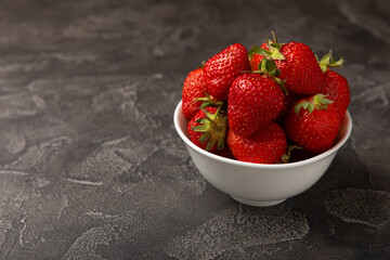 Fresh ripe strawberries in a plate on a black texture background.Vegetarian organic berry.Healthy food.Vitamins.Copy space.Place for text