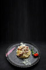 Pasta Carbonara with cheese and tomatoes, on a black plate