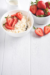 Cottage cheese with strawberries. Breakfast from cottage cheese with slices fresh strawberries, cream, cup of coffee in white bowl on white wooden background. Top view. Food concept. Mock up.