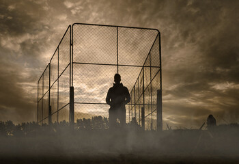 Silhouette of a man standing on sport field on foggy morning. Batting cage. Low angle