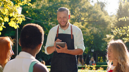 A very good looking waiter with his hair slicked back, is taking down orders in his notebook, he s...