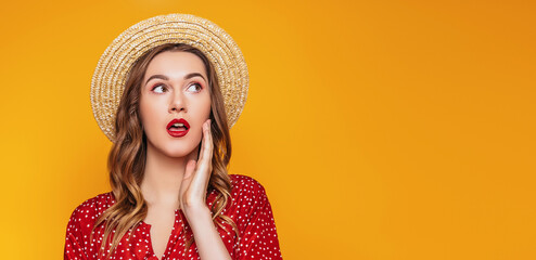 Surprised young girl in a straw hat, in a red dress with a red lipstick looks away at copy space, portrait of a shocked young woman in summer clothes on an orange background, sale concept