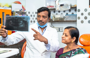 Dentist explaining teeth x-ray report to woman patient at hospital about cavity or dental problems - concept of oral care, expertise and dental care.